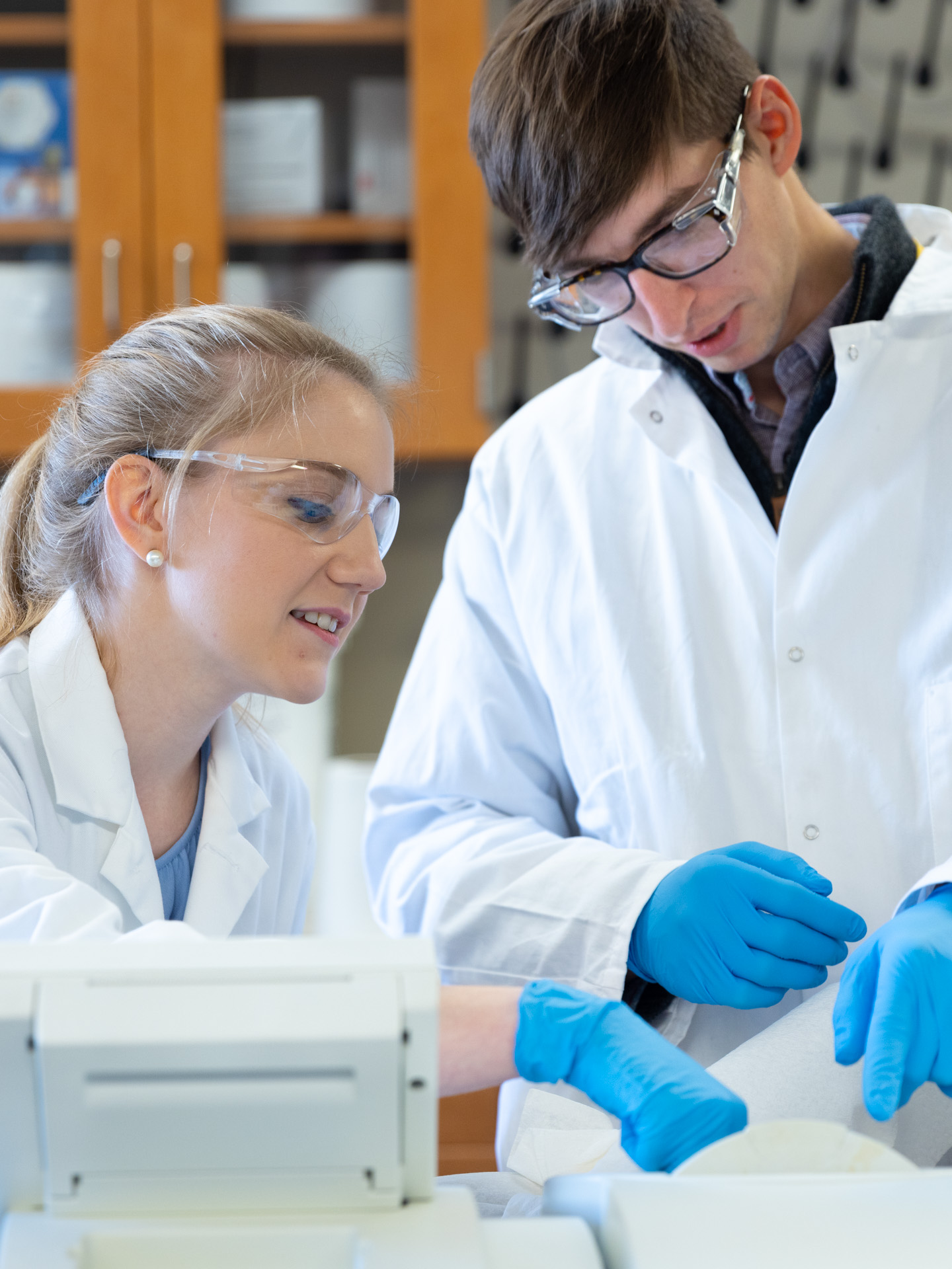 KU Innovation Center-Site Photos-5366 Two young scientists in protective clothing look down at papers at the Business Park in Lawrence